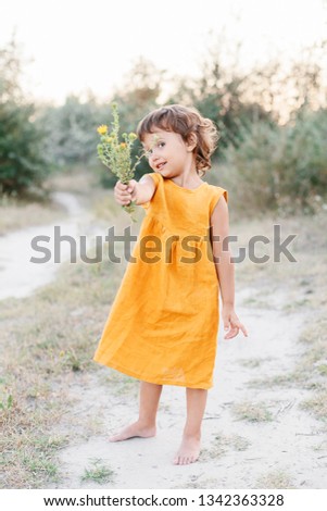 Little girl wearing mustard linen dress holding flowers. Summer vacation. Lifestyle photography