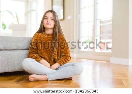 Beautiful young girl kid sitting on the floor at home with serious expression on face. Simple and natural looking at the camera.