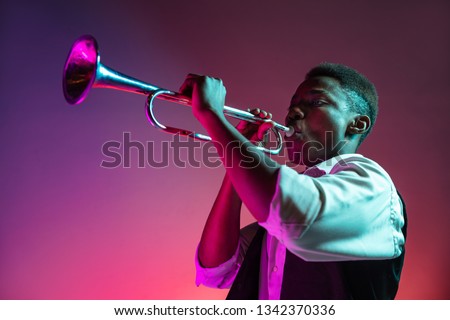 African American handsome jazz musician playing trumpet in the studio on a neon background. Music concept. Young joyful attractive guy improvising. Close-up retro portrait. Royalty-Free Stock Photo #1342370336