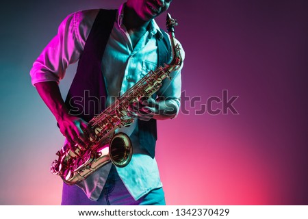 African American handsome jazz musician playing the saxophone in the studio on a neon background. Music concept. Young joyful attractive guy improvising. Close-up retro portrait. Royalty-Free Stock Photo #1342370429