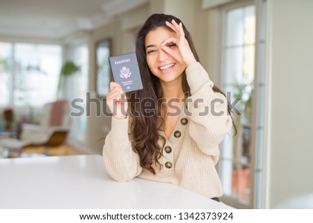 Young woman holding passport of United States of America with happy face smiling doing ok sign with hand on eye looking through fingers