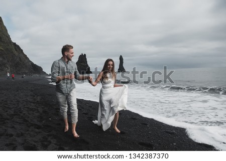 women in white dress is running with her fiance and having fun at the black beach in Iceland