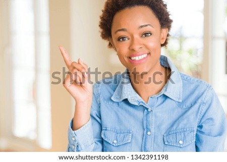 Young beautiful african american woman with a big smile on face, pointing with hand and finger to the side looking at the camera.