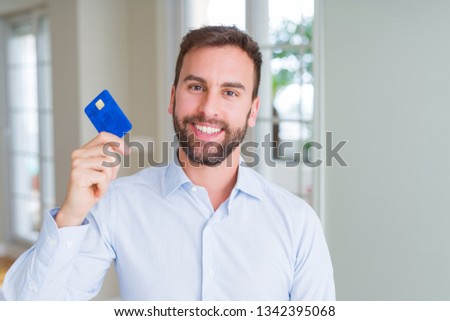 Handsome business man holding credit card with a happy face standing and smiling with a confident smile showing teeth