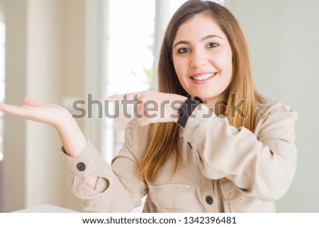 Beautiful young woman at home amazed and smiling to the camera while presenting with hand and pointing with finger.