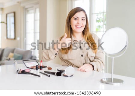 Beautiful young woman using make up cosmetics doing happy thumbs up gesture with hand. Approving expression looking at the camera with showing success.