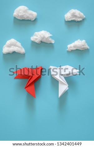 White and red paper pigeons on a blue background among white clouds. Minimal concept