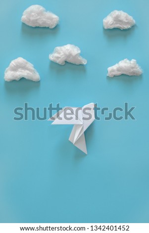 White paper dove on a blue background among the white clouds. Minimal concept