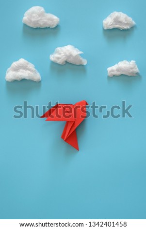 Red origami paper dove on a blue background among the white clouds. Minimal concept