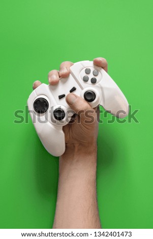 A man's hand holding a white joystick console. Green solid background.