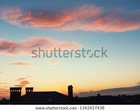 Dark, clear silhouettes of the roofs of houses with chimneys and pipes in the rays of the setting sun. Sunset in the city. Silhouette City landscape in the backlight of the sunset.