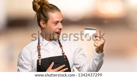 Barber man in an apron holding a credit card and surprised in a barber shop