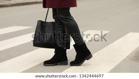 close up of woman legs walking on crosswalk. The woman is wearing black shoes . Handbag in woman hand.