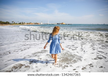 Beautiful girl in blue dress is walking on the beach. Amazing summer photo. Woman near the sea. Holiday travel concept. Slim legs. Warm ocean water.