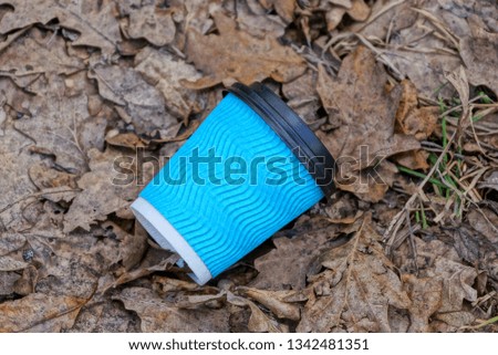 blue paper cup litter lies on dry brown leaves and grass