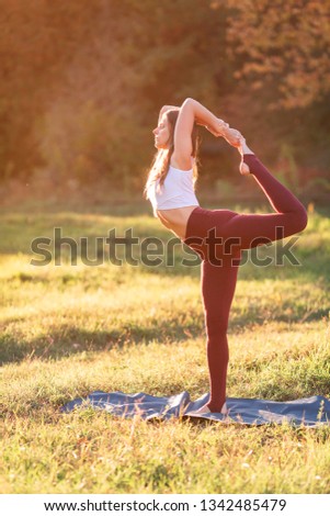 Beautiful young woman practicing yoga at sunset in the park outdoors
