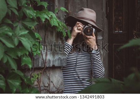 Young beautiful woman in hat is taking picture with old fashioned camera, outdoors