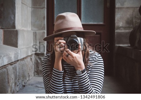 Young beautiful woman in hat is taking picture with old fashioned camera, outdoors