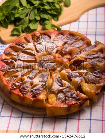Food. Sweet pastries. Round cake with plums and thyme. Pictured with mint, wooden board and knife