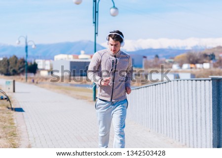 A panting athlete running fast on a track while wearing headphones and grey sweatpants, early in the morning on a sunny day.