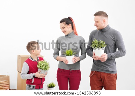 Young family, man woman and child son in new apartments. They are holding green potted plants. Boxes with cargo on a white background. The concept of moving to a new home.