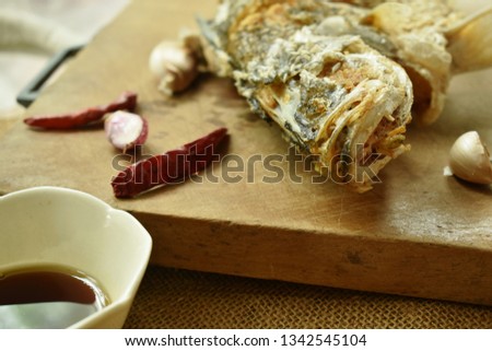 deep fried salty bass fish with soy sauce on wooden chop block