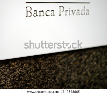 
Selective focus view of a white plate reading 'Banca Privada' in Spanish, private banking services sign on a polished marble dark wall.