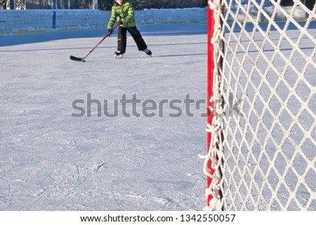 Outdoor ice hockey rink in late afternoon with a single skater practicing his shot to goal in foreground.