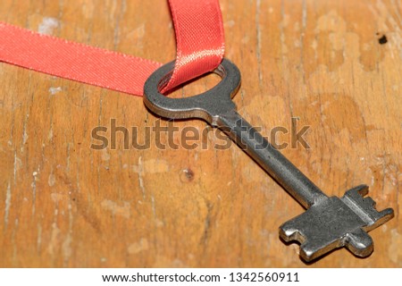The key with the red ribbon is on the wooden table. Close-up image.