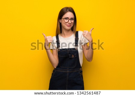 Woman over yellow wall giving a thumbs up gesture and smiling