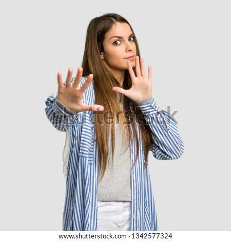 Young girl with striped shirt is a little bit nervous and scared stretching hands to the front over isolated grey background