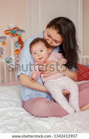 Portrait of beautiful mixed race Asian mother kissing touching embracing her cute adorable newborn infant baby. Early development and health care lifestyle concept. Family in bedroom