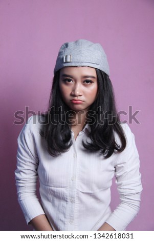 Close up of beautiful Indonesian women's expression with a pink background. the sad and disappointed expression of the woman in the white shirt and the gray hat.