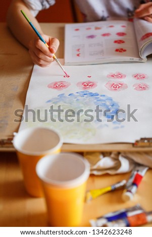 A girl practices watercolor painting of roses with a round brush on a wooden table