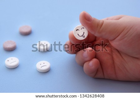 Pills medical. Tablet with smile face in hand. With painted faces and no pictures. A pill with a smile in the foreground against the background of other pills on blue background close-up