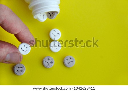 Pills medical. Tablet with smile face in hand. With painted faces and no pictures. A pill with a smile in the foreground against the background of other pills on yellow background close-up