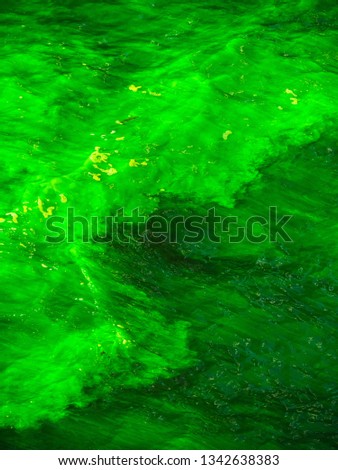 Close up photograph of the Chicago River as clouds of the bright green dye spread and mix throughout the water on St. Patrick's Day holiday during annual celebrations and festivities in downtown.