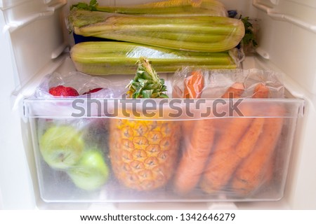 Colorful fruits and vegetables in fridge crisper - apples, pineapple, carrots, celery