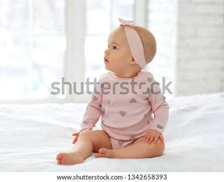 Cute 8-month-old baby with a headband on a white bed in pink clothes Royalty-Free Stock Photo #1342658393