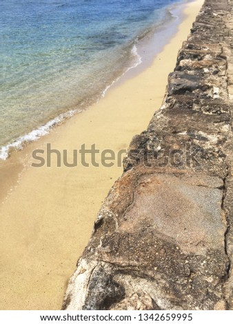 White sand beach with gentle tropical waves washing on the beach, next to a volcanic rock wall near Waikiki, Oahu, Hawaii.