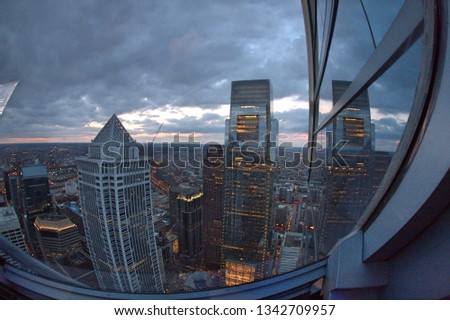Wide angle image of skyscraper glass with building reflection and cityscape of high rise buildings, skyscrapers and cityscape in Philadelphia, Pennsylvania at sunset with orange sky behind gray clouds