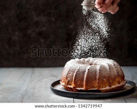 Woman's hand sprinkling icing sugar over fresh bundt cake. Powder sugar falls on fresh perfect bundt cake. Copy space for text. Ideas and recipes for breakfast or dessert. Black background