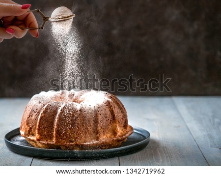 Woman's hand sprinkling icing sugar over fresh bundt cake. Powder sugar falls on fresh perfect bundt cake. Copy space for text. Ideas and recipes for breakfast or dessert