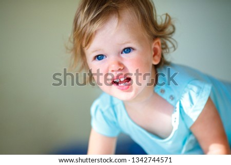 Lovely toddler girl with curly blonde hair indoors. A child showing emotions of sadness and resentment