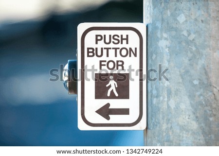 Crosswalk button on a light pole for pedestrian crossing with an icon and text