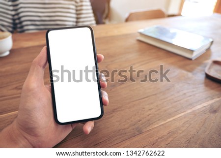 Mockup image of a man's hand holding black mobile phone with blank screen with woman in cafe