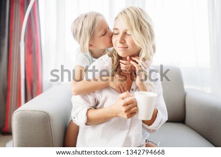 Daughter kisses mom sitting on the couch