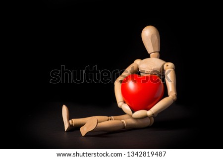 Wooden puppet with a big red heart in his hands on a black background