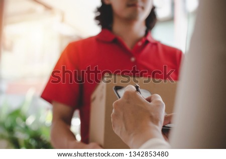 young woman customer appending signature in digital mobile phone receiving parcel post box from courier with home delivery service man in red uniform at home, express delivery, online shopping concept