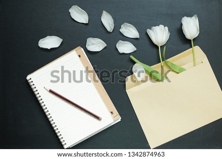  Back to school composition. An envelope with flowers next to a paper blank on a dark desk background. White tulips, pencil, space for notes. Flat lay, top view,  copy space.